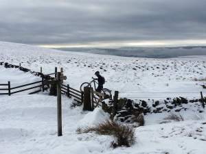 A mountain biker near Lose Hill in the Peak District carries their bike over a blanket of snow.